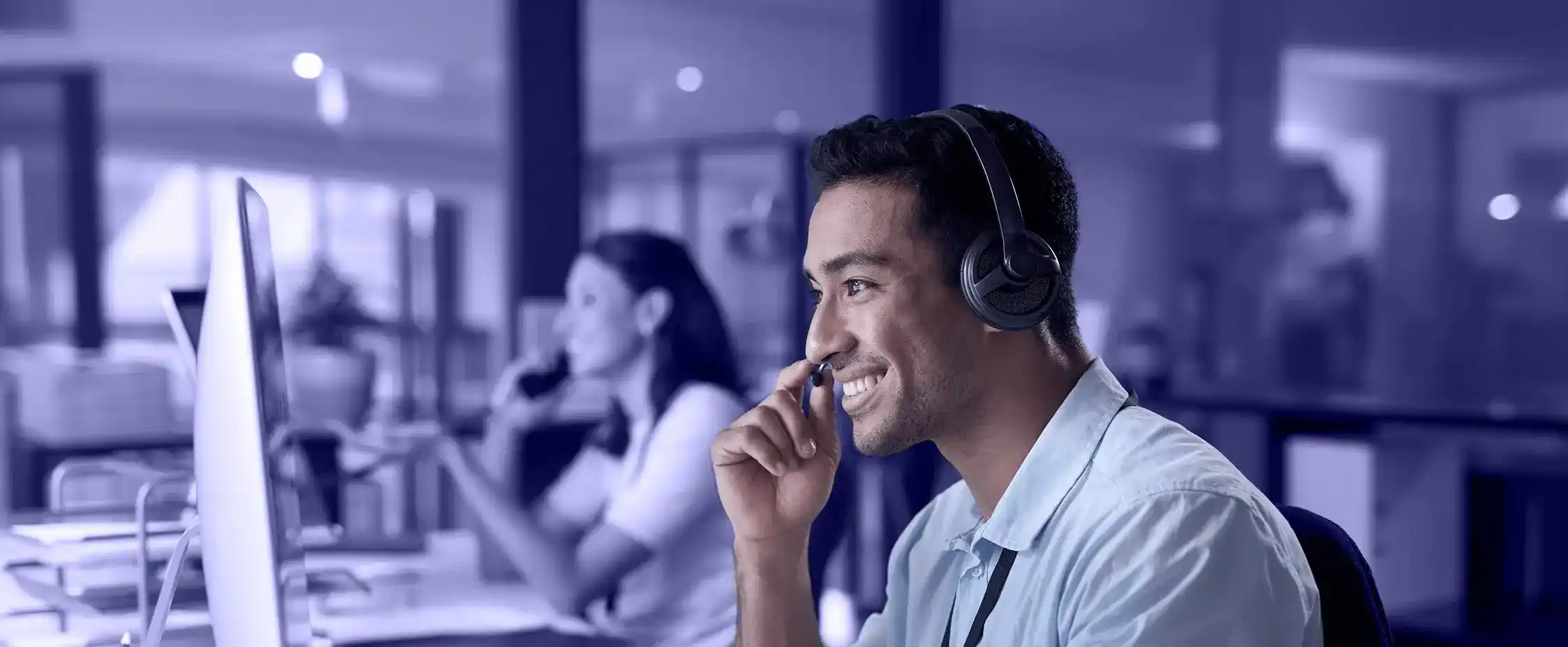 Smiling customer support agent wearing a headset in a modern office.